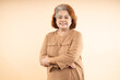 © GAJENDRRA BHATI  - Portrait of smiling senior Indian woman standing cross arms isolated on beige background.