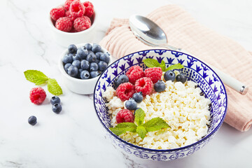 Canvas Print - Cottage cheese in bowl decorated with raspberries and blueberries and mint leaves on white