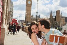 Couple, travel and selfie with kiss outdoor in London for romantic holiday, adventure and love in city street. Man, woman and smartphone, happiness with smile in traveling photo, tourist and romance.