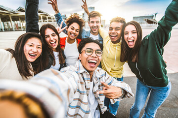 Wall Mural - Multicultural happy friends having fun taking selfie group photo portrait outside - University students smiling together at camera in college campus - Teenagers hanging out on city street