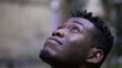 Pensive young black man meditating outdoors. African person face close-up looking up at sky