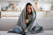 © DimaBerlin - Sick exhausted woman with thermometer to measure body temperature sit on sofa at home wrapped in blanket. Suffering depressed girl experiences health problems due to abnormally cold winter weather