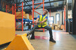 Asian male warehouse worker pulling a pallet truck. Worker working with hand pallet truck unloading cargo boxes on pallet at the warehouse.