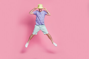 Wall Mural - Full length photo of attractive young guy jump pull hat tongue out spread legs dressed trendy blue outfit isolated on pink color background