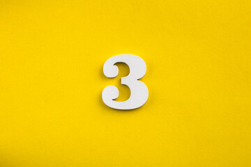 number three - white number in wood on yellow background
