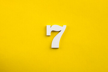 number seven - white number in wood on yellow background