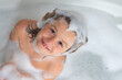 Kids shampoo. Foam on child head. Kid having fun in the bath with bubbles. Happy child enjoying bath time. Little boy smiling in the bath with soap foam. Child bathes in a bath with foam.