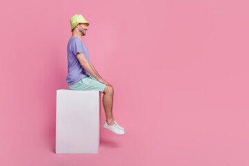 Sticker - Full size photo of handsome young guy sitting profile big white platform ad dressed trendy blue clothes isolated on pink color background