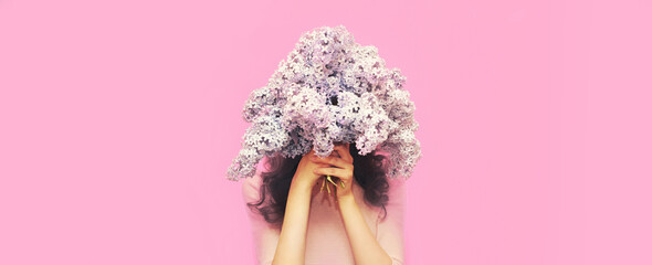 Portrait of woman covering her head with bouquet of fresh lilac flowers on pink background