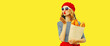 Portrait of beautiful woman blowing her red lips sending sweet air kiss holding grocery shopping paper bag with long white bread baguette wearing french red beret isolated on yellow background