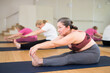 Active elderly woman practicing stretching yoga postures on mat at group class