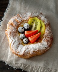 Sticker - Vertical closeup shot of a gourmet round croissant pastry with powdered sugar and fruits