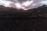 Fototapeta Mapy - Wild volcanic desert landscape with dark mountains and fog,  Jandía peninsula in Fuerteventura, Spain