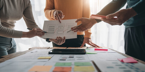 Close up ux developer and ui designer brainstorming about mobile app interface wireframe design on table with customer breif and color code at modern office.Creative digital development agency