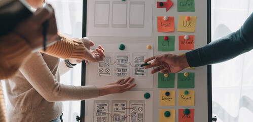 Close up ux developer and ui designer brainstorming about mobile app interface wireframe design on table with customer breif and color code at modern office.Creative digital development agency