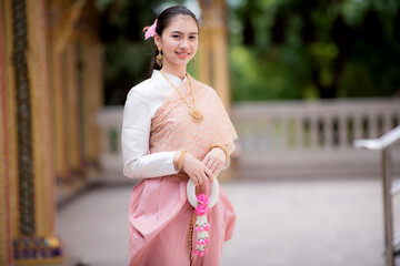 Wall Mural - Portrait of a beautiful woman wearing a traditional Thai dress smiling gracefully standing in a temple of Thailand