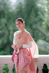 Wall Mural - Portrait of a beautiful woman wearing a traditional Thai dress smiling gracefully standing in a temple of Thailand