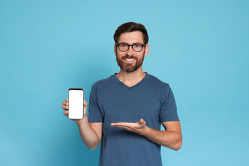 Happy man showing smartphone on light blue background