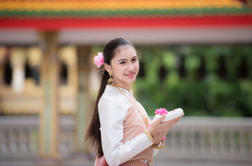 Wall Mural - Portrait of a beautiful woman wearing a traditional Thai dress smiling gracefully standing in a temple of Thailand