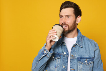 Poster - Handsome bearded man drinking from paper cup on orange background. Space for text