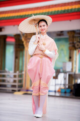 Wall Mural - Portrait of a beautiful woman wearing a traditional Thai dress smiling gracefully standing in a temple of Thailand