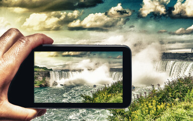 Wall Mural - Female hand with smartphone taking a picture of Niagara Falls. Tourism concept.