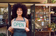 © C Haas/peopleimages.com - Open sign, black woman and garden shop owner of a small business manager portrait happy. Smile of a retail store entrepreneur with welcome shopping board and business owner with plant products
