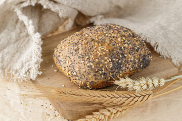 Wall Mural - Fresh baked wheat bun with poppy and sesame seeds and ears closeup on wooden board.