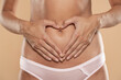 © vladimirfloyd - Partial view of beautiful slim woman in underwear posing with heart shape hands near belly isolated on beige background