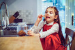 Happy cute little girl kid standing on the chair and eating festive gingerbread cookies from just reached jar on the shelf on decorated for winter Christmas holidays modern kitchen. Overeating sweets.