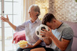 © luciano - Caucasian couple of young soccer fan and elderly grandmother with disappointed expression while watching soccer match on tv sitting on comfortable sofa in living room