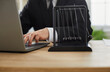 © Studio Romantic - Businessman working on laptop computer at his desk with Newton's cradle. Close up of Newton's pendulum on office table of man typing on notebook PC keyboard. Cropped shot, closeup. Business background