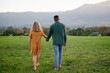 © StratfordProductions - Rear view of young multiracial couple holding hands while walking in field