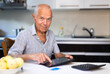 © caftor - Grandfather man doing online payment from digital tablet. Elderly senior caucasian grandpa paying bills online