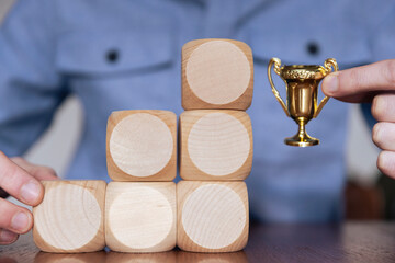 Wall Mural - Business person arranging large wooden blocks with a winning trophy. Business success