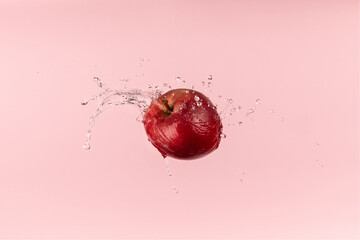 Fresh red apple on pink background with water splash