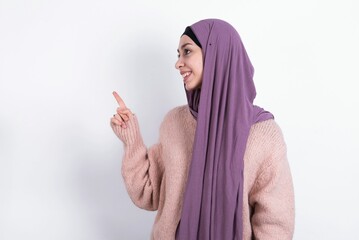 muslim woman wearing hijab and knitted sweater over white background looking at camera indicating finger empty space sales