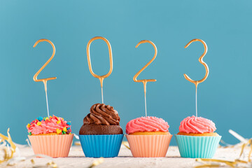 Holiday muffins with pink butter cream and 2023 numbers on blue background. Happy New Year theme.