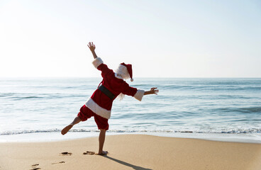 Santa claus standing on beach with arms outstretched.