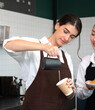 © Nassorn - Professional female barista pouring milk into hot drink coffee cup making cappuccino or latte for a morning caffeine drink. Woman wearing apron standing at counter in cafe preparing hot beverage.
