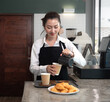 © Nassorn - Professional female barista pouring milk into hot drink coffee cup making cappuccino or latte for a morning caffeine drink. Woman wearing apron standing at counter in cafe preparing hot beverage.
