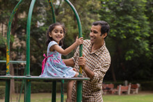 Little Girl Playing On The Merry Go Round With Her Father In The Park