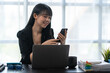© crizzystudio - Asian businesswoman in formal suit in office happy and cheerful during using smartphone and working