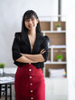 © crizzystudio - Portrait of successful confident pretty, young Asian businesswoman or freelancer standing near work desk in office, wearing formal stylish clothes, arms crossed, looking at camera, smiling friendly