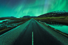 Polar Lights Sparkling Over Asphalt Road Surrounded With Mountains In Iceland