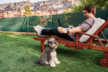 Man Working On Laptop While Playing With Dog In Yard