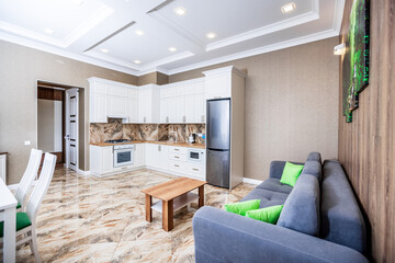 Wall Mural - studio kitchen in apartments in a modern style. white kitchen with wooden countertop. White dining table with white chairs. Brown sofa.