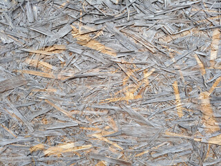 Fragment of the surface of an old fibreboard. Individual wooden chips are visible. The wood has dried and become partly gray with time. Background. Texture.