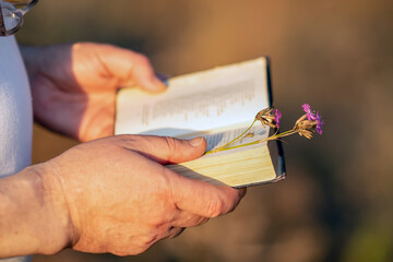 A caucasian man holds an old book in his hand on a bright sunny day. Close-up with a blurred background.