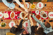 Christmas, high five and food with a group of friends sitting around a dinner table together for celebration. Thanksgiving, hands and meal with a team enjoying a lunch on a wooden surface from above